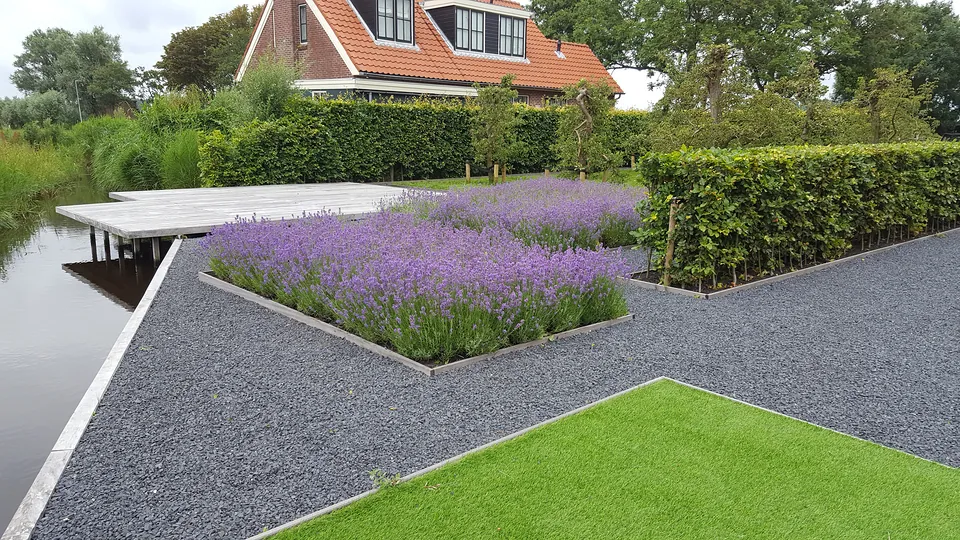 Borders met lavendel tussen antraciet grindpaden, met gazon en hagen bij het water