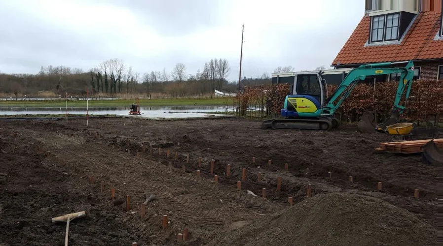 De tuin vóór de aanleg: kale grond, uitgezette paaltjes en een graafmachine